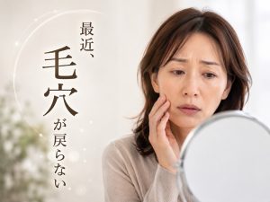 鏡を見ながら頬の毛穴を気にする40代女性。毛穴の開きや乾燥に悩む様子のイメージ画像